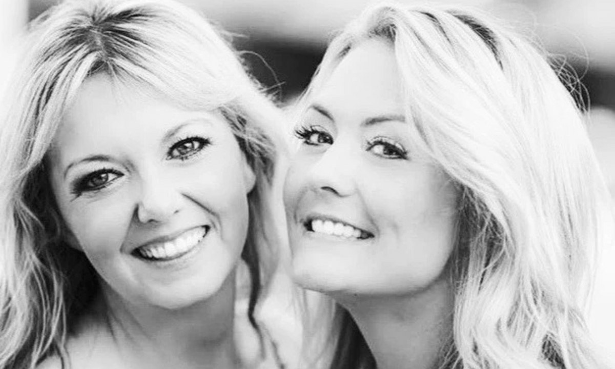 Black and white portrait of two smiling women with long blonde hair, posing cheek to cheek
