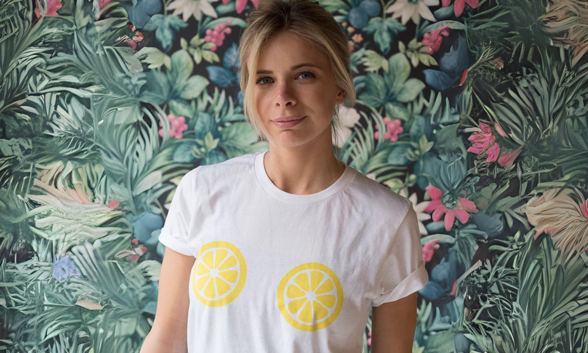 Woman in a white T-shirt printed with two lemon slices across the chest, in front of tropical leaf wallpaper
